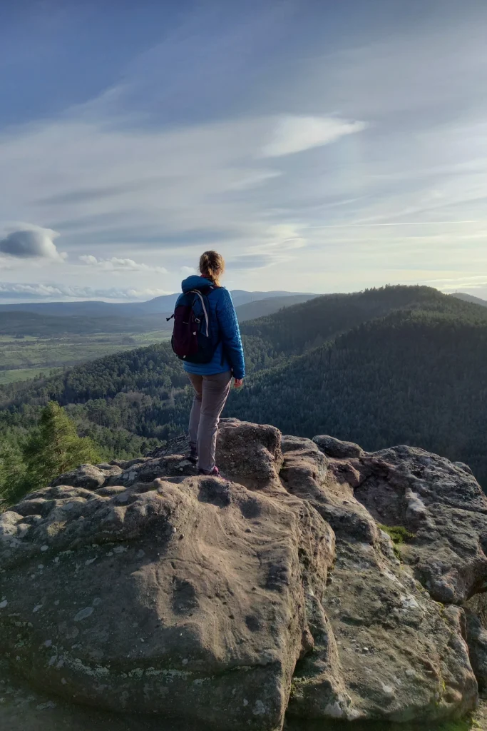 Une randonneuse au rocher du Brotsch qui regarde la forêt et sommets vosgiens