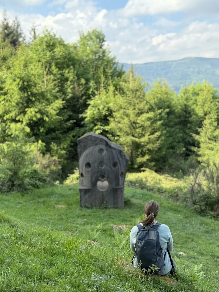 Une randonneuse assise face à la sculpture Porte du Cosmos, sur les hauteurs de Wisches dans la vallée de la Bruche
